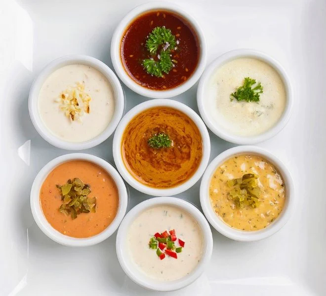 A white plate topped with seven different types of soup.