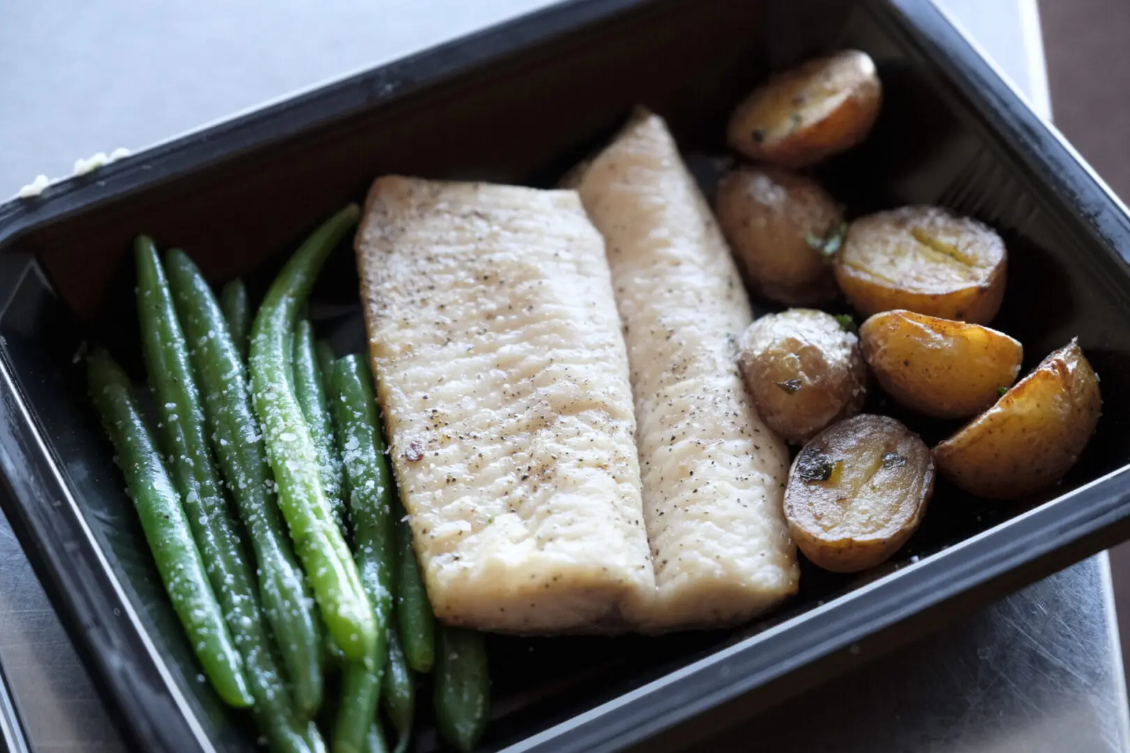 A tray of food with fish, potatoes and green beans.