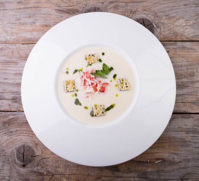 A white plate topped with soup on top of a wooden table.